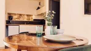 Une table de salle à manger ronde en bois, sur laquelle se trouvent une assiette blanche, deux verres transparents et un vase avec des feuilles vertes.
