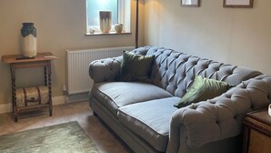 A cozy living room with a grey sofa, a wooden side table, a floor lamp, and framed artwork on the wall. - THE PIGGERY CHESHIRE. The perfect place to get away from it all (Smallwood)