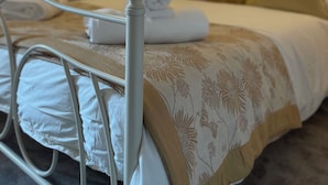 A neatly made bed with white linens and a floral-patterned duvet, a bedside table with a lamp, and a wall-mounted artwork. - THE PIGGERY CHESHIRE. The perfect place to get away from it all (Smallwood)