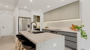 Une cuisine moderne dotée d’un îlot central, d’appareils électroménagers en acier inoxydable et d’un design minimaliste.