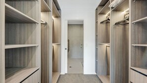 Un dressing accessible sans porte, doté de nombreuses étagères et d’un espace pour suspendre les vêtements, avec une porte au fond et un sol recouvert de moquette.