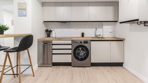 Una cocina compacta con armarios blancos, lavavajillas, lavadora y encimera de madera.