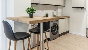 Una cocina moderna con encimera de madera, dos sillas negras, una lavadora y una pequeña planta en maceta.