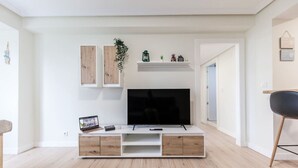 Una sala de estar moderna con un televisor de pantalla plana sobre un mueble blanco, armarios de madera y una silla negra.