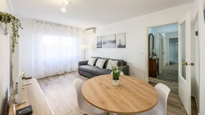 A modern living room with a grey sofa, a round wooden dining table, and a white coffee table. - Family-Friendly Stay near Madrid (San Sebastián de los Reyes)