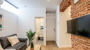 A modern living room with a sofa, a coffee table, and a TV mounted on a brick wall. - Urban Tranquility in Madrid - Ideal for Couples (Madrid)