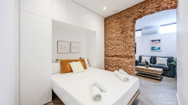 A modern bedroom with a brick wall, a bed with white linens, a sofa, and a coffee table. - Urban Tranquility in Madrid - Ideal for Couples (Madrid)
