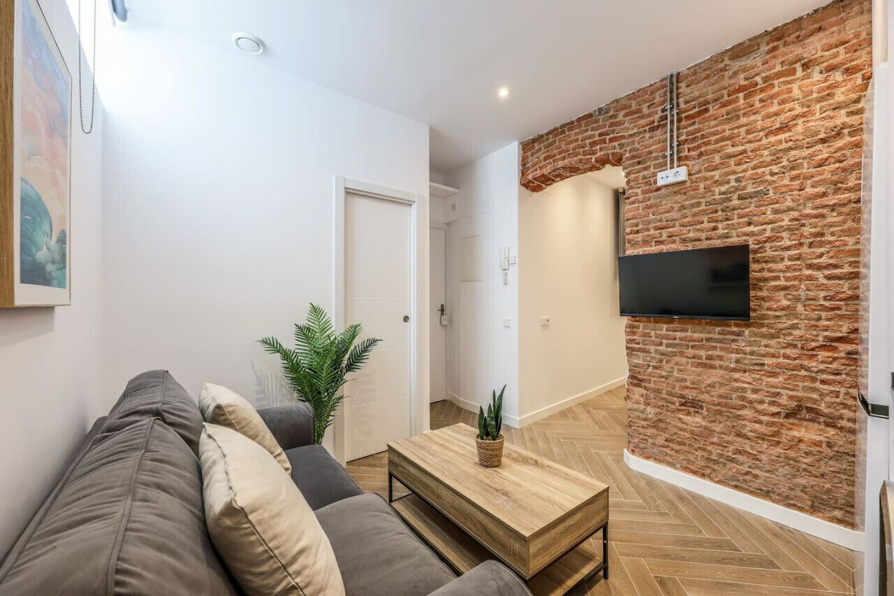 Un salon moderne avec un canapé, une table basse et un téléviseur fixé au mur, qui est en briques.