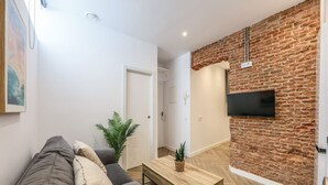 A modern living room with a sofa, a coffee table, and a TV mounted on a brick wall. - Urban Tranquility in Madrid - Ideal for Couples (Madrid)