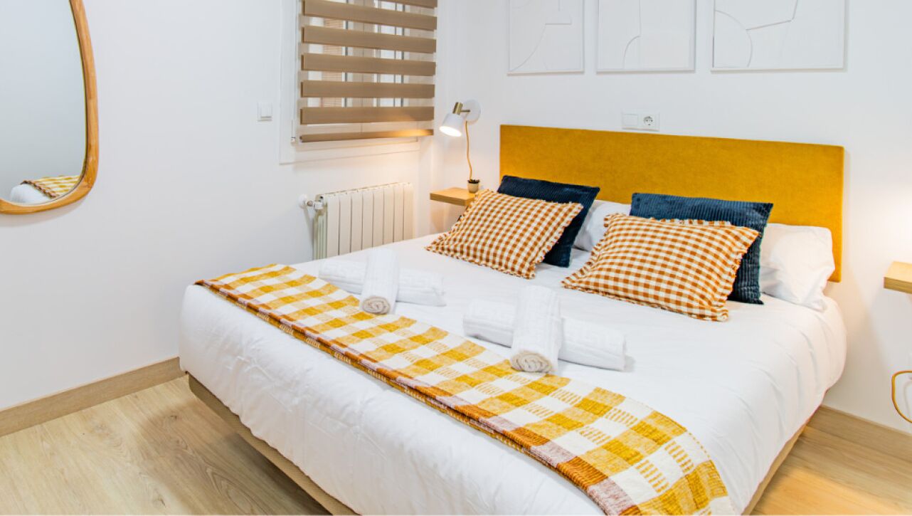 Una cama bien hecha con un edredón de cuadros, una lámpara de noche y un cabecero de madera.