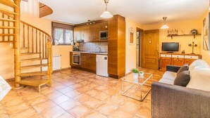 A modern kitchen with wooden cabinets, a built-in oven, and a refrigerator. There is a dining area with a sofa and a coffee table. A spiral staircase leads to an upper level. - Rural Duplex in the Pyrenees - Garden and Parking (Senegüé)