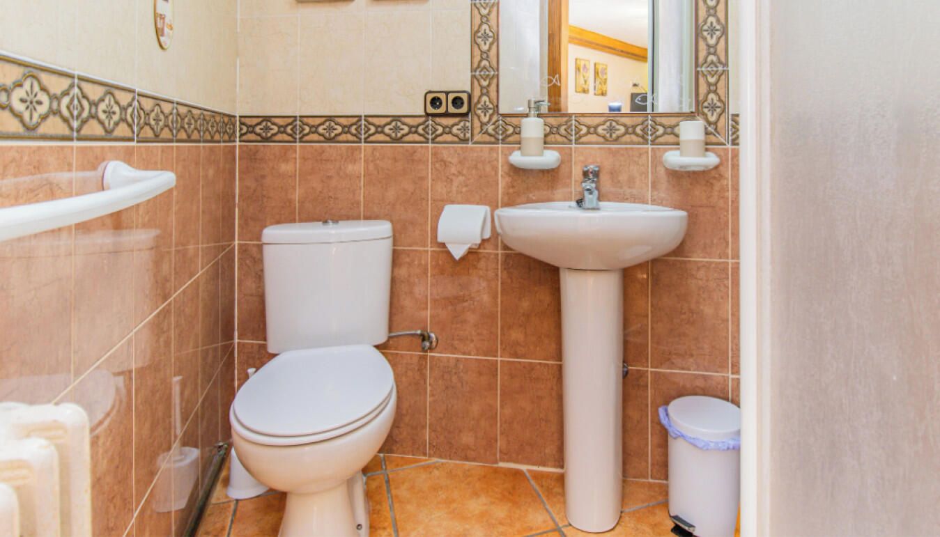 Un baño con inodoro, lavamanos y un cubo de basura.