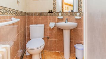 Un baño con inodoro, lavamanos y un cubo de basura.