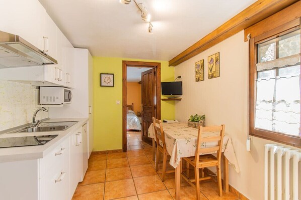 A compact kitchen with white cabinets, a microwave, and a sink. There's a dining area with a table and chairs, and a TV on the wall. - Apartment for Couples in the Pyrenees - Garden & Parking (Senegüé)