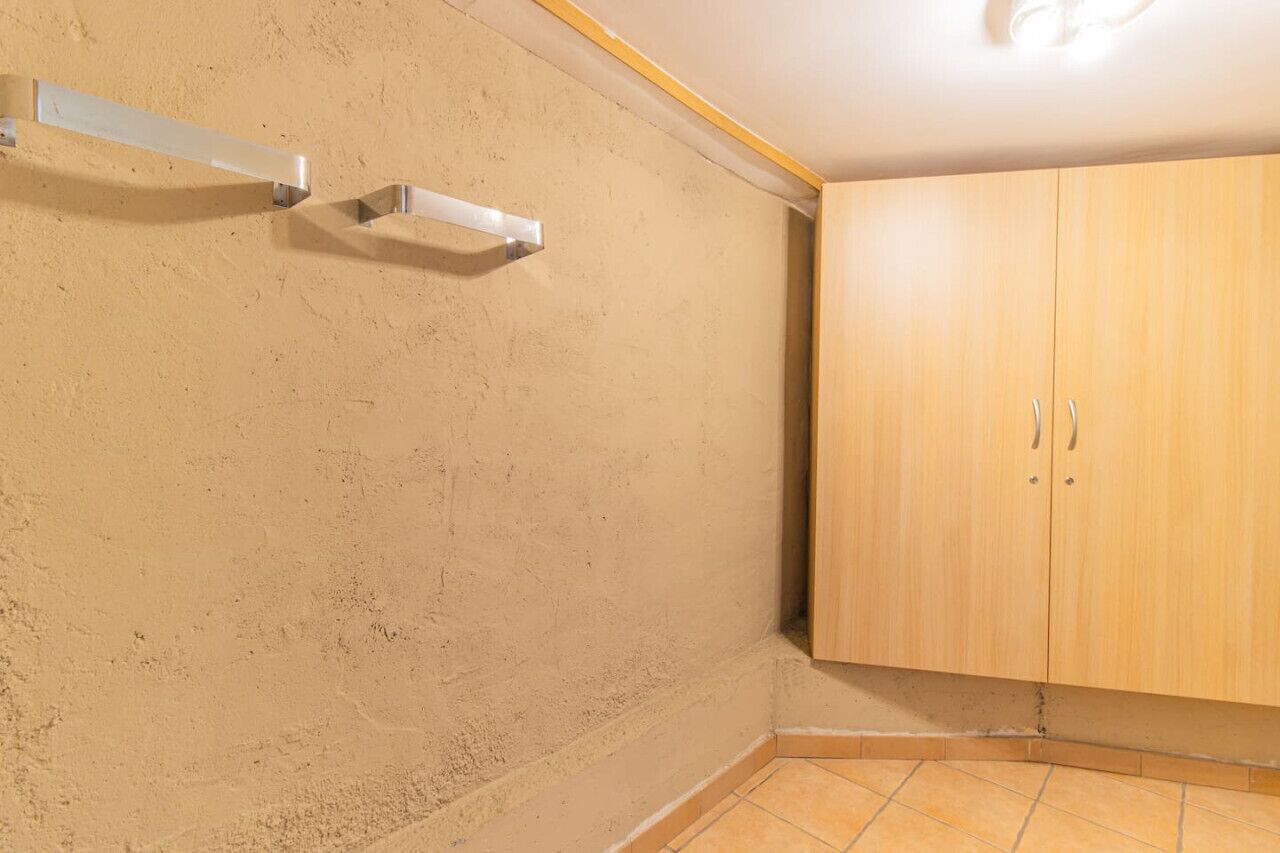 Una habitación de esquina con un armario de madera, un estante blanco y una pared beige con textura.