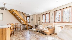 A spacious living area with a wooden staircase, a sofa set, a coffee table, and a dining area with chairs. - Rustic Duplex in the Pyrenees - Garden & Parking (Senegüé)