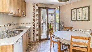 A kitchen with wooden cabinets, a double sink, and a dining area with a round table and chairs. - Rustic Duplex in the Pyrenees - Garden & Parking (Senegüé)