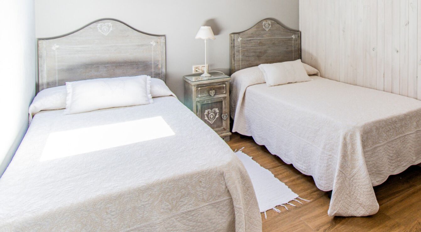 Una habitación con dos camas individuales, una mesita de noche con lámpara y un cabecero de madera.