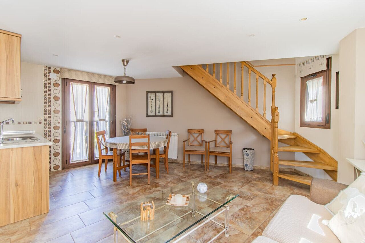 A spacious living area with a wooden staircase, a dining table with chairs, and a glass coffee table.