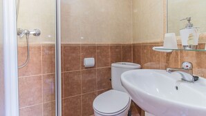 A bathroom with a glass shower enclosure, a white toilet, and a sink with a soap dispenser.