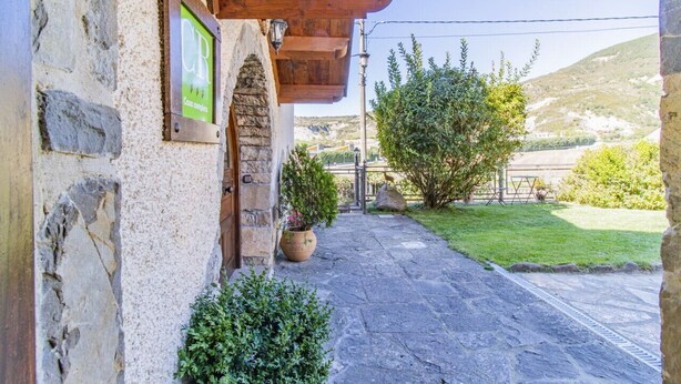 A stone building with a wooden pergola entrance, a potted plant, and a clear view of the surrounding landscape.
