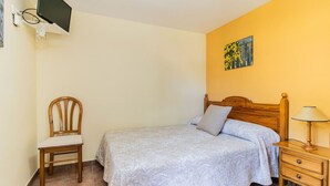 A bedroom with a bed, a chair, a nightstand, and a wall-mounted TV.