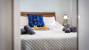 Un lit bien fait, recouvert d’une couverture matelassée, un oreiller bleu orné d’un motif floral, un plateau avec des croissants et du jus d’orange, et une lampe de chevet.