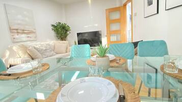Een moderne woonkamer met een glazen eettafel, teal stoelen en een bank met een plant.