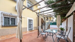 En gårdsplads med et glasbord, stole, en pergola og en trappe til en etage ovenover.