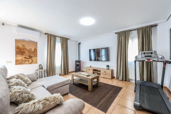 A living room with a sofa, coffee table, TV, treadmill, and a painting on the wall.