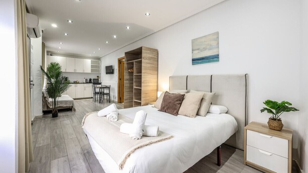 A modern hotel room with a large bed, a bedside table, a small desk, and a kitchenette in the background. - Classy Studio close to Retiro Park, Madrid (Madrid)