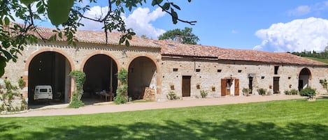 Un bâtiment en pierre doté de plusieurs arcades et d’un toit en tuiles, entouré d’une pelouse bien entretenue.