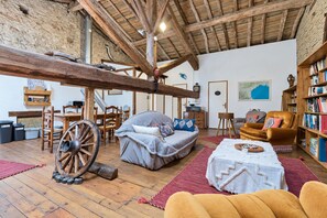 A rustic interior with exposed wooden beams, a large wooden wheel, a sofa, a chair, and a bookshelf. - Spacious 190 m² Holiday Home, Billiards, Memorable Gatherings near Canal du Midi (lagarde)