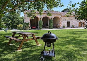 A patio with a wooden table and a portable grill, set against a stone building with arches. - Spacious 190 m² Holiday Home, Billiards, Memorable Gatherings near Canal du Midi (lagarde)