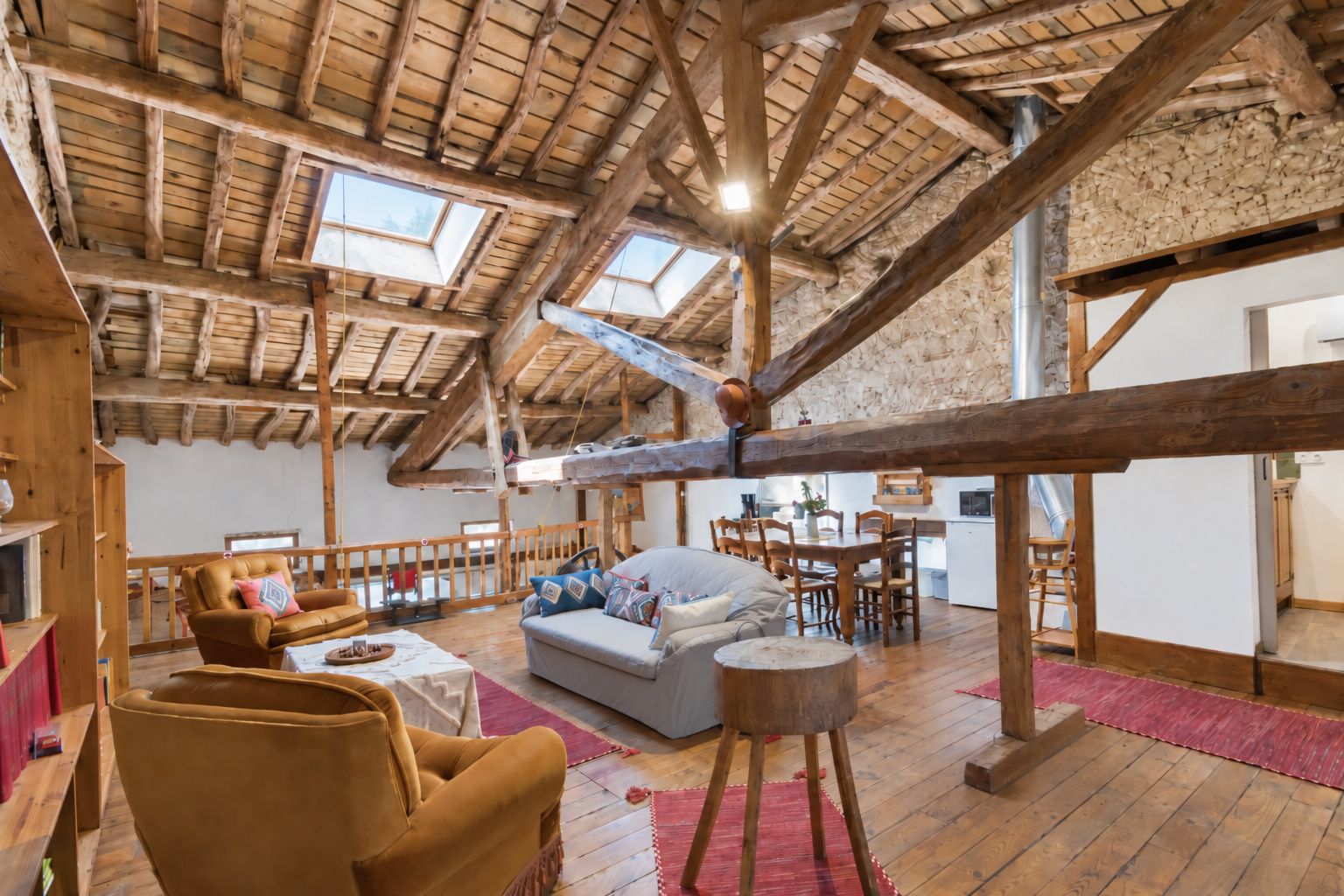 Un loft espaiós amb un alt sostre de fusta, una zona de seients acollidora amb un sofà i butaques, i una taula de dinar.