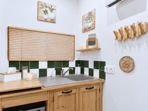 A kitchen with a wooden countertop, a sink, and a window with blinds. There are two wall-mounted shelves, one with a candle and a mirror, and another with wooden utensils. - Spacious 190 m² Holiday Home, Billiards, Memorable Gatherings near Canal du Midi (lagarde)