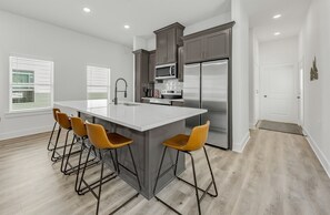 A modern kitchen with a large island, bar stools, and stainless steel appliances. - Midtown: New Home, 2 Miles to A&M/TV in Every Room (Bryan)