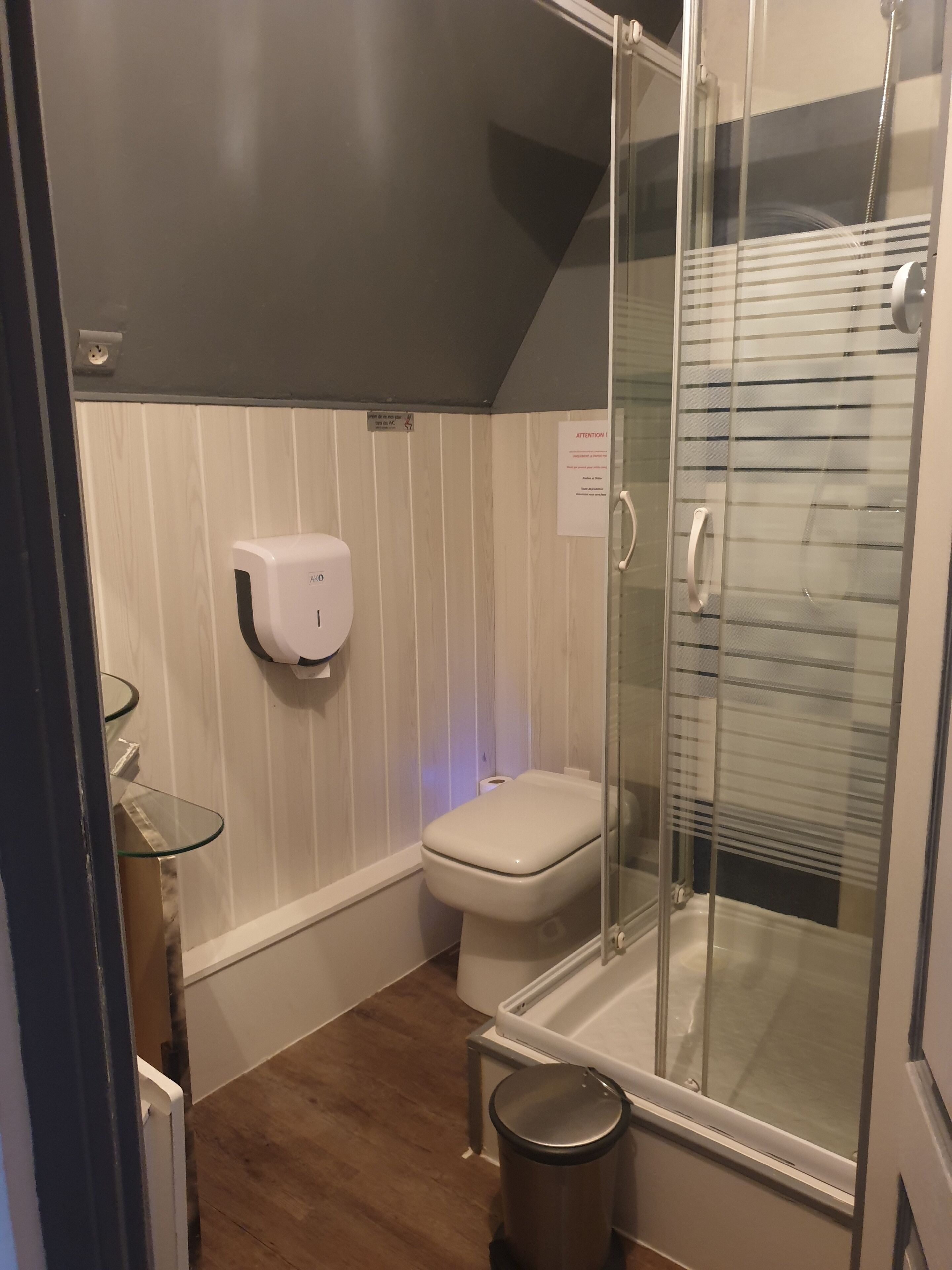 A compact bathroom with a glass shower enclosure, a toilet, and a hand soap dispenser.