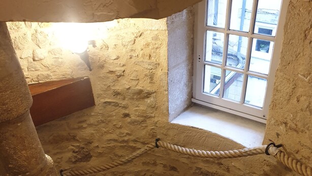 A stone spiral staircase in a rustic room with a window overlooking a street. - L (Saint-Amand-Montrond)