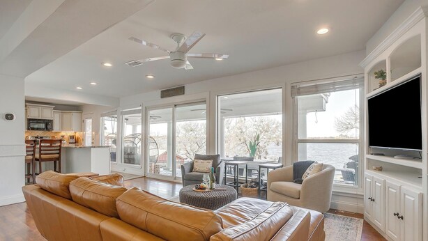 A spacious living room with a leather sofa, a television, and a kitchen in the background.