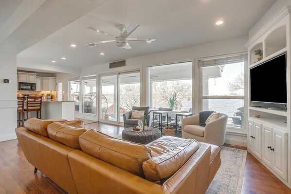 A spacious living room with a leather sofa, a television, and a kitchen in the background.