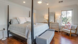 A four-poster bed with a bench, a chair, a dresser, and a mirror in a bedroom with wooden flooring and a ceiling fan.
