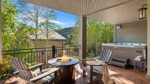 Eine Terrasse mit Feuerschale, zwei Adirondack-Stühlen, einem Whirlpool und Blick auf einen Berg.
