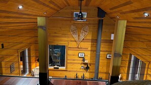 Un interior de madera con techo inclinado, chimenea y un ventanal grande.