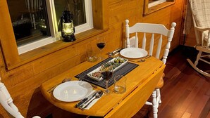 Una mesa de madera para comer con sillas blancas, una vela y una copa de vino.