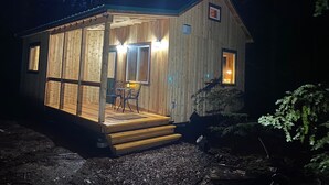 Una cabaña de madera pequeña con un porche, una mesa y dos sillas.