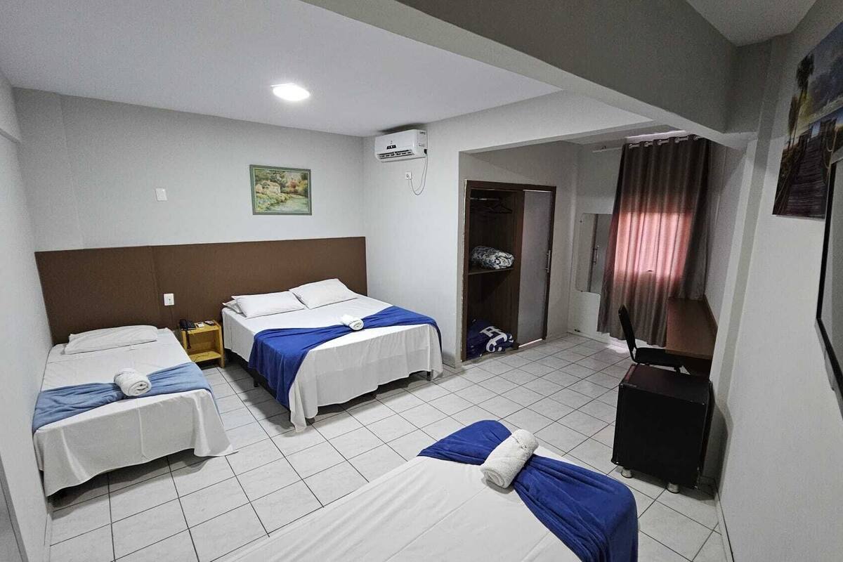 A hotel room with two single beds, a desk, a chair, a TV, and an air conditioning unit.