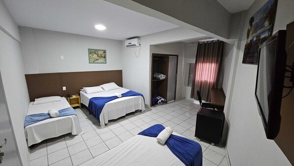 A hotel room with two single beds, a desk, a chair, a TV, and an air conditioning unit.