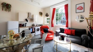 A modern living room with a glass coffee table, a red armchair, a black sofa, and a dining area with a glass table. - STR8BS8 Banksy 2-Bedroom Apartment, Clifton, Parking & Garden (Redland)