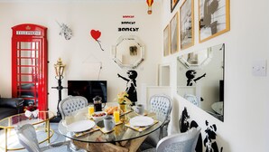 A dining area with a glass table, chairs, and a red telephone booth. - STR8BS8 Banksy 2-Bedroom Apartment, Clifton, Parking & Garden (Redland)